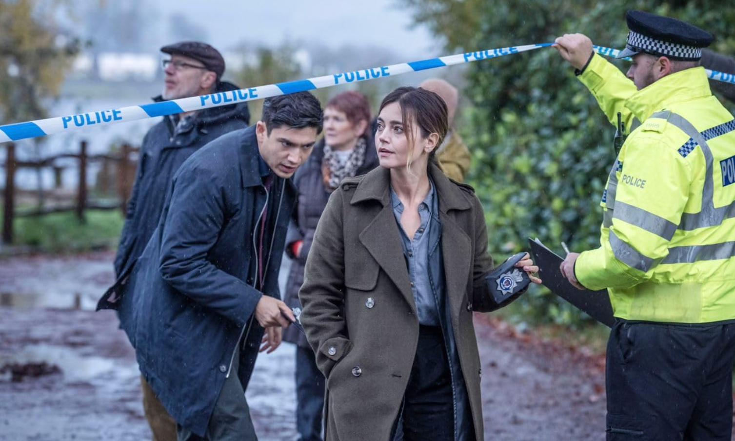 a woman in trench coat holding a police tape over a group of people