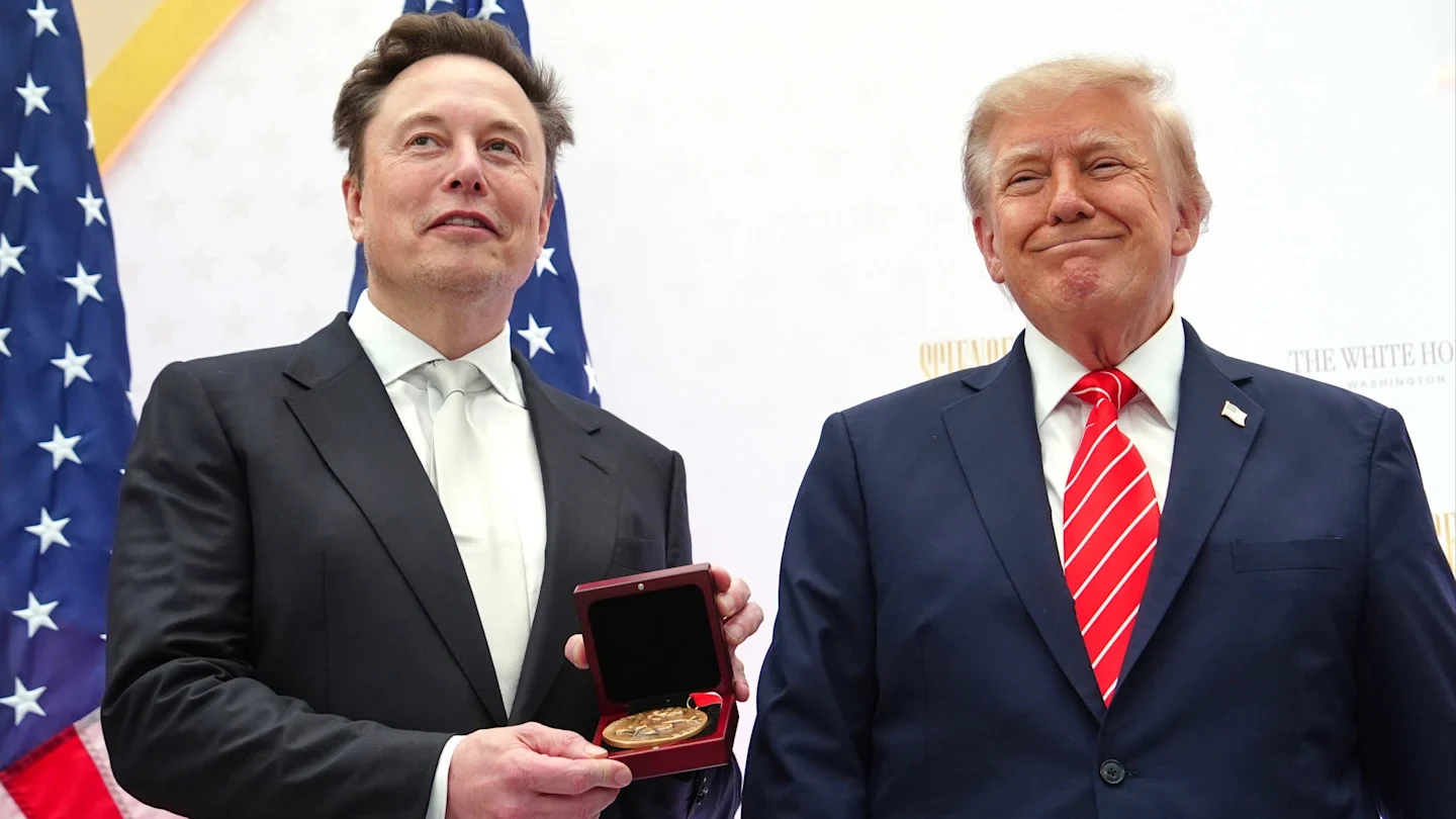 Elon Musk holds the National Medal of Science next to President Donald Trump, both standing in front of American flags.